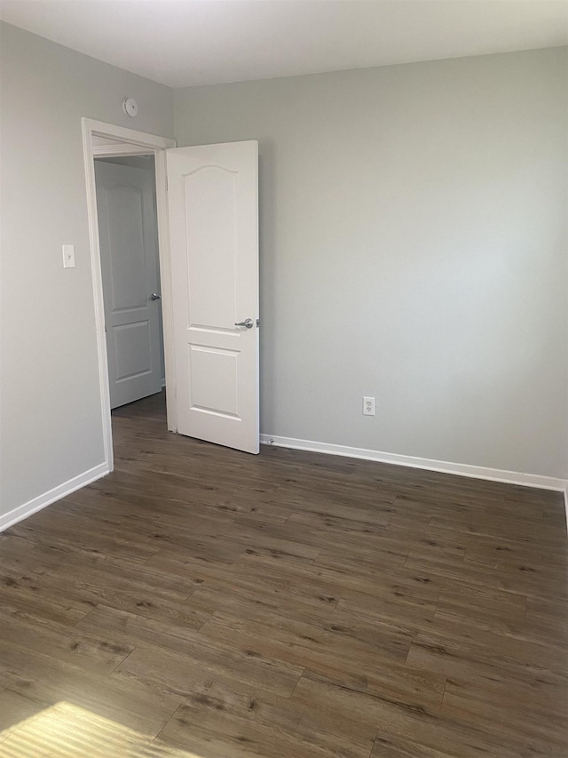 unfurnished room featuring baseboards and dark wood-style flooring