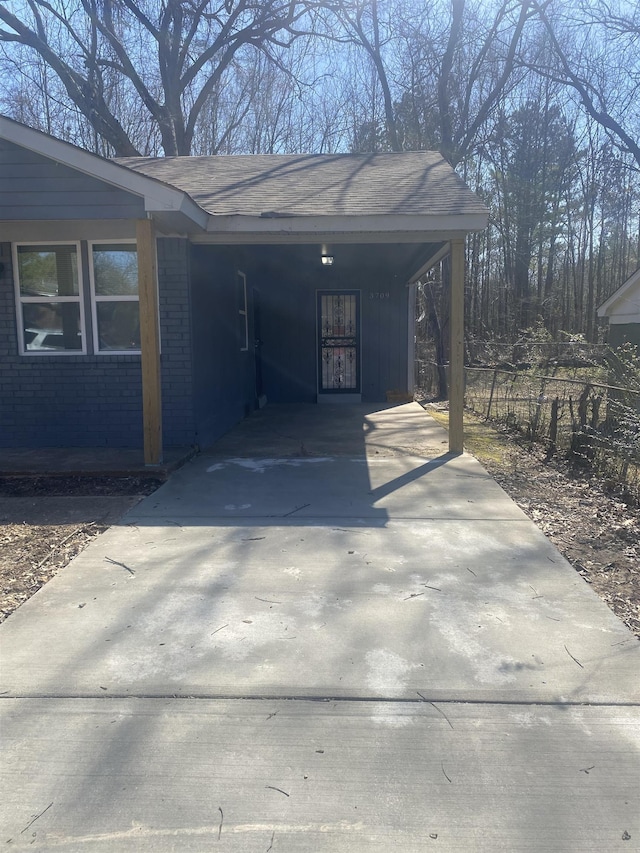 view of car parking featuring driveway, fence, and a carport