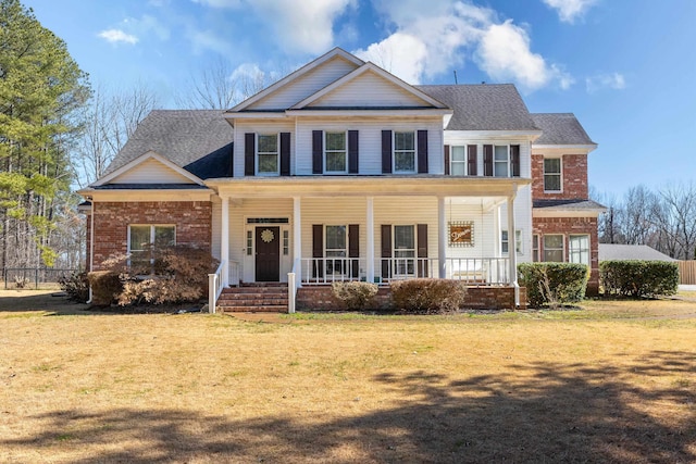 view of front facade featuring a porch, a front lawn, a shingled roof, and brick siding