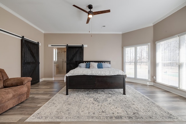 bedroom with a barn door, baseboards, visible vents, ornamental molding, and wood finished floors