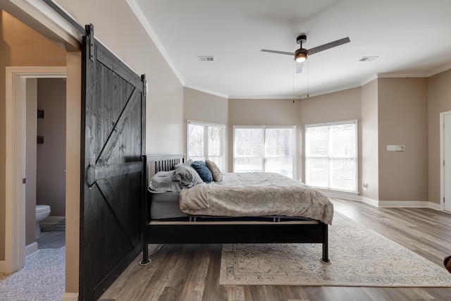 bedroom with a barn door, crown molding, visible vents, and wood finished floors