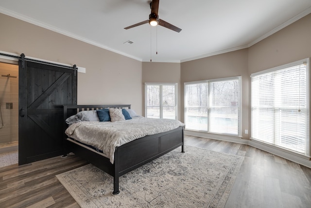 bedroom featuring a barn door, multiple windows, ornamental molding, and wood finished floors