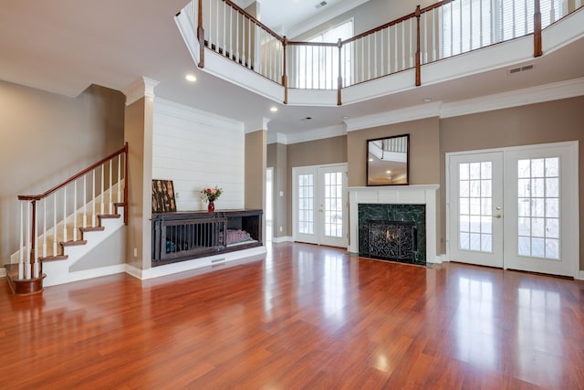 unfurnished living room with a high ceiling, wood finished floors, french doors, and a high end fireplace