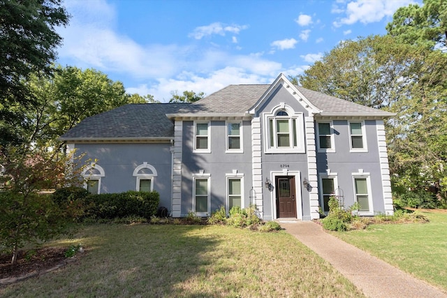 colonial house with roof with shingles, a front lawn, and stucco siding