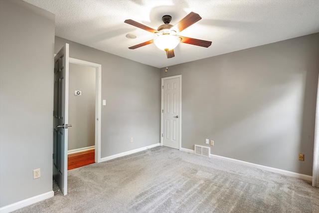 spare room featuring carpet floors, visible vents, a textured ceiling, and baseboards
