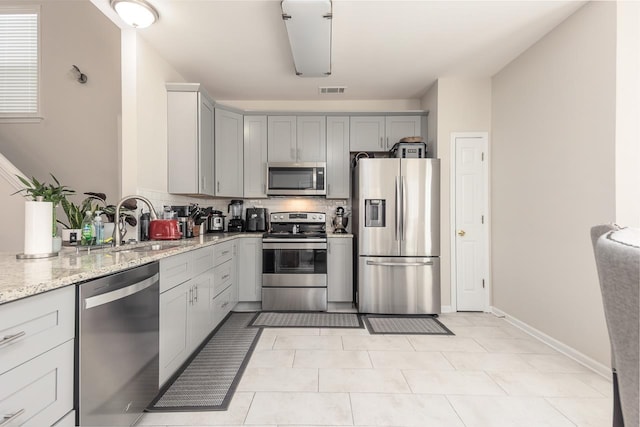 kitchen featuring tasteful backsplash, appliances with stainless steel finishes, light stone countertops, gray cabinets, and a sink