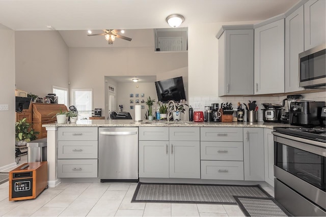 kitchen featuring light stone counters, a peninsula, gray cabinets, stainless steel appliances, and a sink