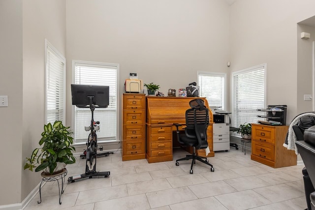 office featuring a towering ceiling, baseboards, and light tile patterned flooring