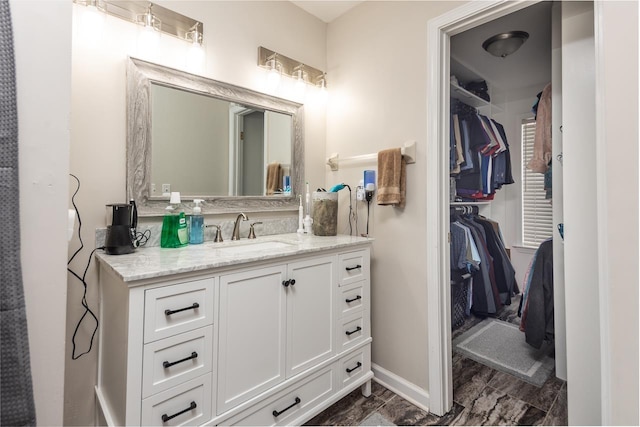 bathroom featuring vanity, baseboards, and a spacious closet