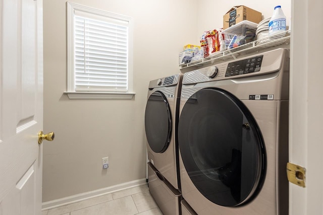 clothes washing area featuring light tile patterned floors, laundry area, washing machine and dryer, and baseboards