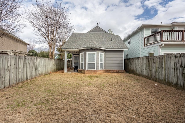 back of house featuring roof with shingles, a lawn, and a fenced backyard