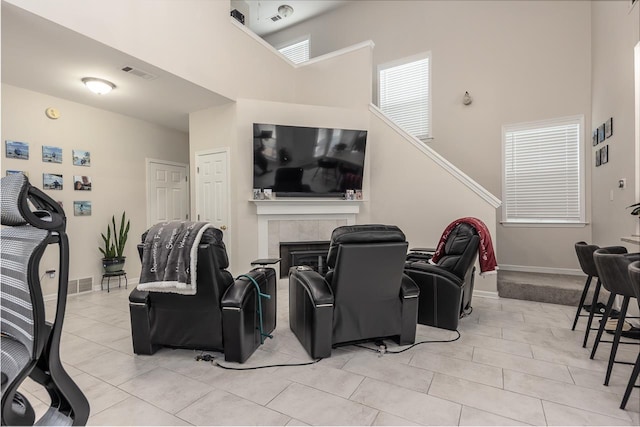 home theater featuring light tile patterned floors, baseboards, visible vents, a tiled fireplace, and a towering ceiling