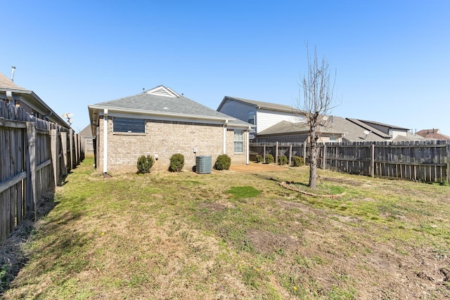 rear view of house featuring a fenced backyard, a lawn, central AC, and brick siding