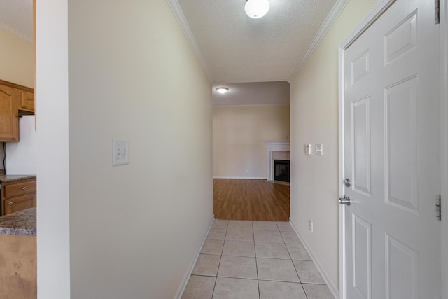 corridor with a textured ceiling, ornamental molding, light tile patterned flooring, and baseboards