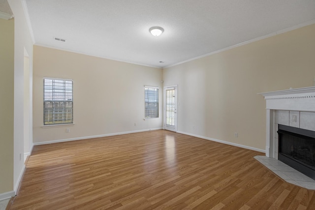 unfurnished living room with light wood-type flooring, a tile fireplace, visible vents, and crown molding