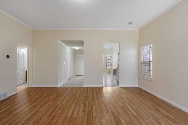 empty room with light wood-style floors, visible vents, baseboards, and crown molding