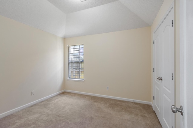 empty room with lofted ceiling, a textured ceiling, baseboards, and light colored carpet