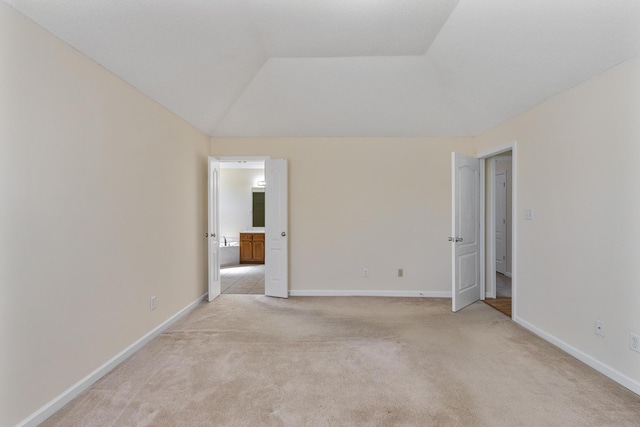 spare room with baseboards, vaulted ceiling, and light colored carpet