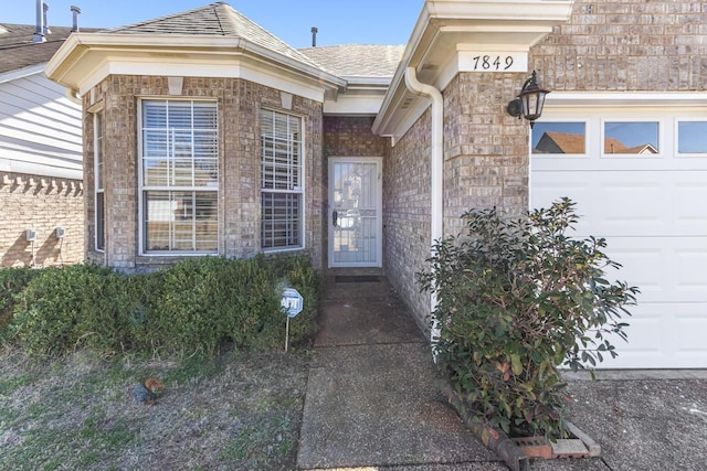 view of exterior entry with brick siding and an attached garage