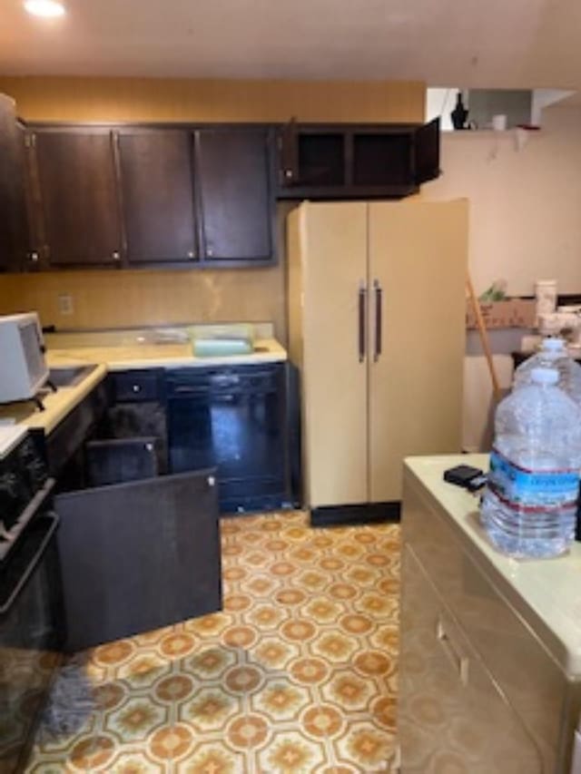 kitchen with freestanding refrigerator, oven, light countertops, and dark brown cabinets