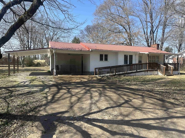 view of front of home featuring an attached carport, metal roof, driveway, and a chimney