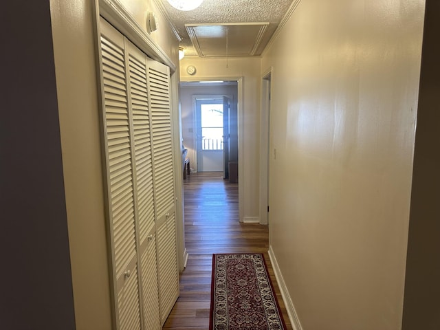 corridor with crown molding, attic access, dark wood-type flooring, a textured ceiling, and baseboards