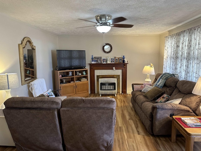 living room with a textured ceiling, ceiling fan, a fireplace, and wood finished floors