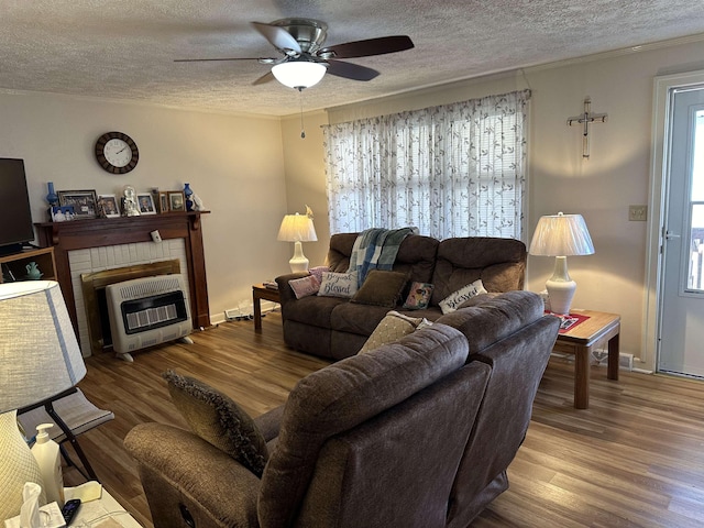 living area featuring a ceiling fan, wood finished floors, heating unit, a textured ceiling, and a brick fireplace