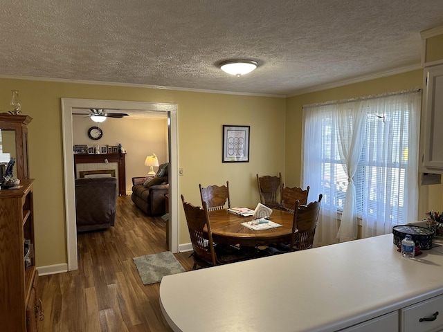 dining room featuring ceiling fan, a textured ceiling, baseboards, dark wood-style floors, and crown molding