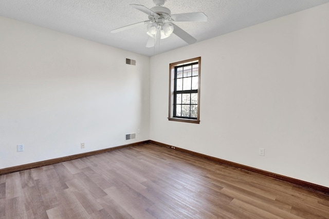 spare room featuring a textured ceiling, wood finished floors, visible vents, and baseboards