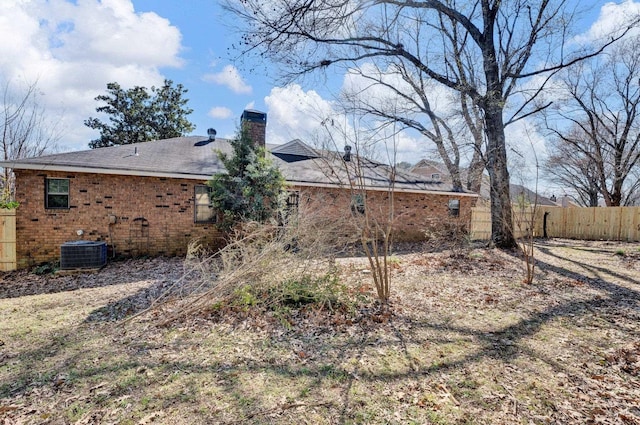 rear view of house with brick siding, fence, a chimney, and central AC unit