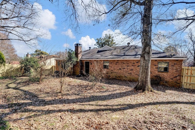 rear view of house featuring a chimney, fence, and brick siding