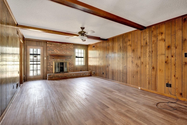 unfurnished living room featuring beam ceiling, a brick fireplace, wood walls, a textured ceiling, and wood finished floors