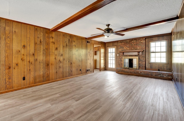 unfurnished living room featuring a textured ceiling, a brick fireplace, wood finished floors, and beam ceiling