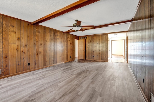 unfurnished room with beamed ceiling, wood walls, a textured ceiling, and wood finished floors