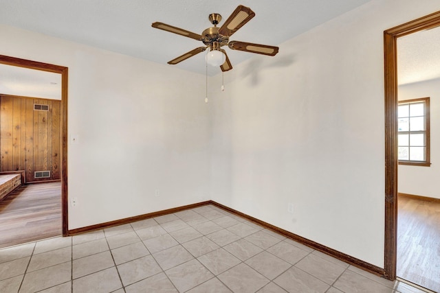 spare room featuring light wood-style flooring, visible vents, ceiling fan, and wooden walls