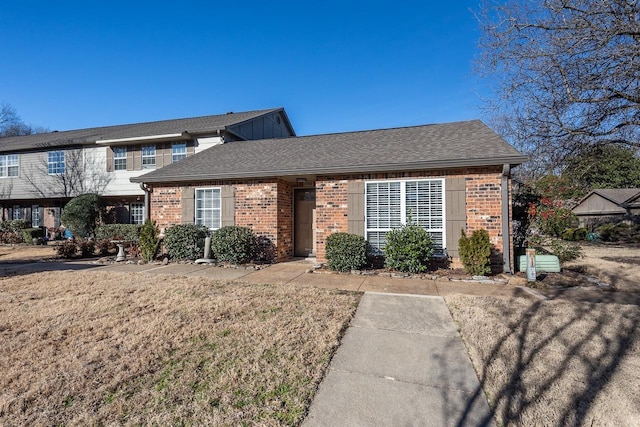 view of front of property featuring brick siding, a front lawn, and roof with shingles