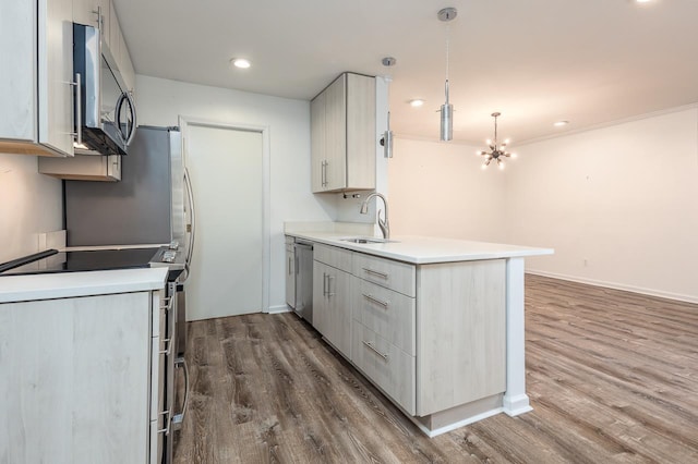 kitchen with dark wood finished floors, appliances with stainless steel finishes, a peninsula, light countertops, and a sink