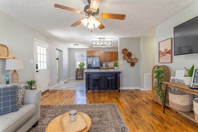 living area with baseboards, light wood-style flooring, visible vents, and a textured ceiling