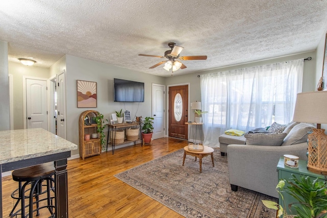 living area with ceiling fan, a textured ceiling, wood finished floors, and baseboards