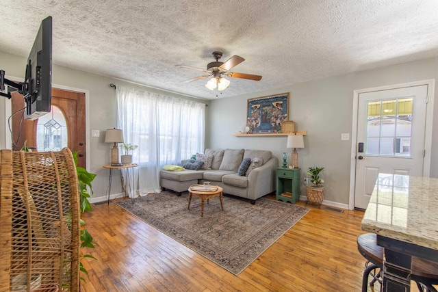 living area featuring light wood-type flooring, ceiling fan, a textured ceiling, and baseboards