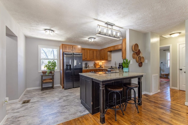 kitchen featuring visible vents, brown cabinetry, stainless steel fridge with ice dispenser, a peninsula, and light wood-style floors