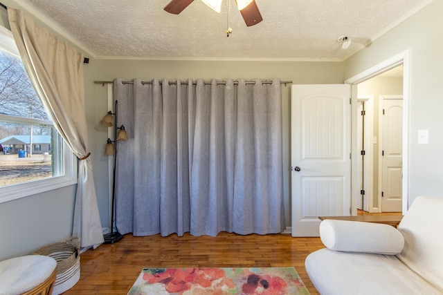 interior space with a textured ceiling, ornamental molding, wood finished floors, and a ceiling fan