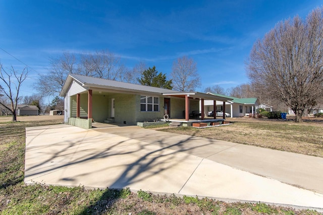 ranch-style home featuring driveway, metal roof, an attached carport, and a front yard