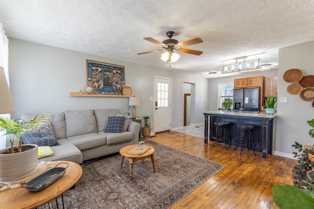 living area featuring baseboards, a textured ceiling, a ceiling fan, and light wood-style floors