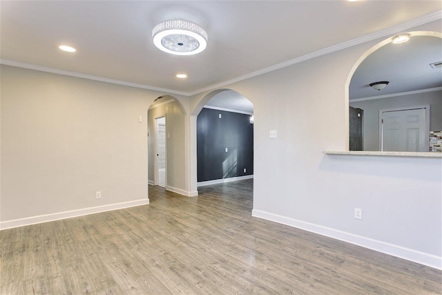 spare room featuring ornamental molding, arched walkways, baseboards, and wood finished floors