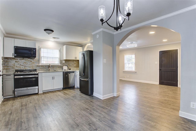 kitchen featuring arched walkways, backsplash, appliances with stainless steel finishes, ornamental molding, and a sink