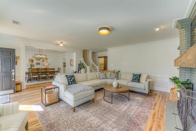 living room with a brick fireplace, visible vents, crown molding, and wood finished floors