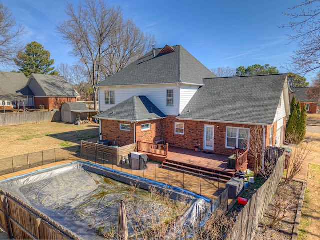 back of property with a deck, fence private yard, brick siding, a yard, and roof with shingles