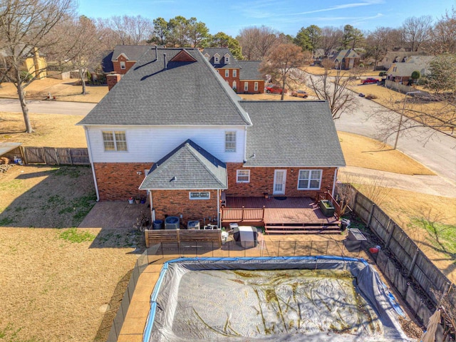 exterior space with a fenced backyard, brick siding, roof with shingles, a lawn, and a wooden deck